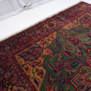 May include: A vintage Persian rug with a green, red and yellow geometric pattern. The rug has a fringed border and is made of wool.