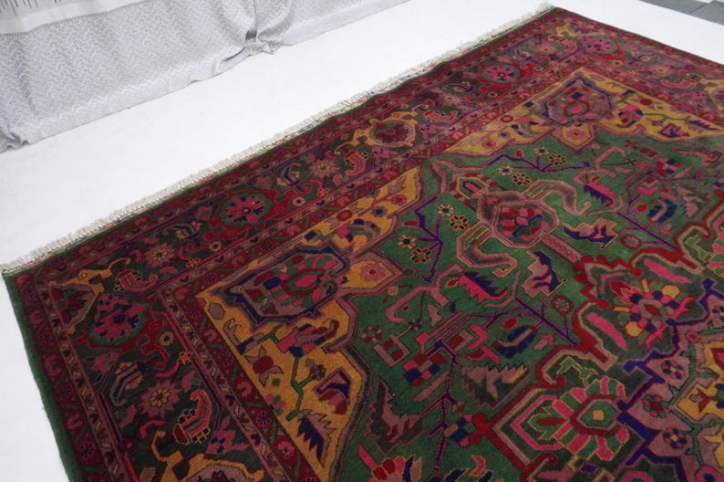 May include: A vintage Persian rug with a green, red and yellow geometric pattern. The rug has a fringed border and is made of wool.