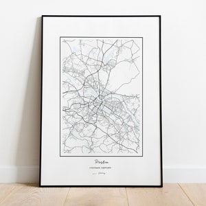 Könnte beinhalten: Ein gerahmter Schwarz-Weiß-Kartendruck von Dresden, Deutschland. Die Karte zeigt die Straßen und Wasserwege der Stadt. Der Name der Stadt ist unten aufgedruckt, mit zusätzlichem Text. Der Druck wird auf einem hellen Holzboden angezeigt.