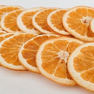 May include: A collection of dried orange slices arranged in rows. The slices are a warm orange color with a lighter, almost white, outer ring. The image is taken from a slightly elevated angle, showcasing the texture and detail of the fruit.