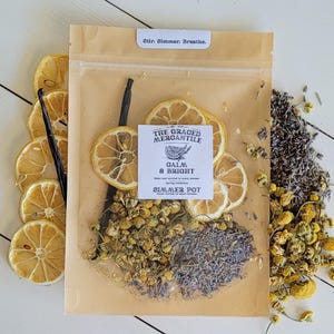 May include: A cellophane bag containing dried lemon slices, vanilla bean, chamomile, and lavender. The bag has a label that reads "THE GRACED MERCANTILE CALM & BRIGHT SIMMER POT". The top of the bag reads "Stir. Simmer. Breathe."