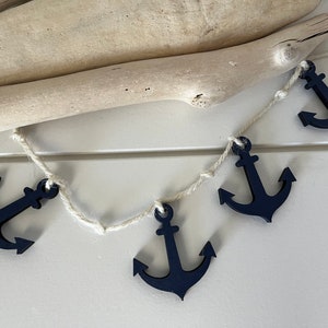 May include: A navy blue anchor garland with white twine. The garland is hanging from a piece of driftwood.
