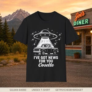 May include: A black short-sleeve t-shirt featuring a white graphic of a pickup truck being beamed up by a UFO. The design includes the text I'VE GOT NEWS FOR YOU Cosette in a bold white font, surrounded by small star accents on a dark background.