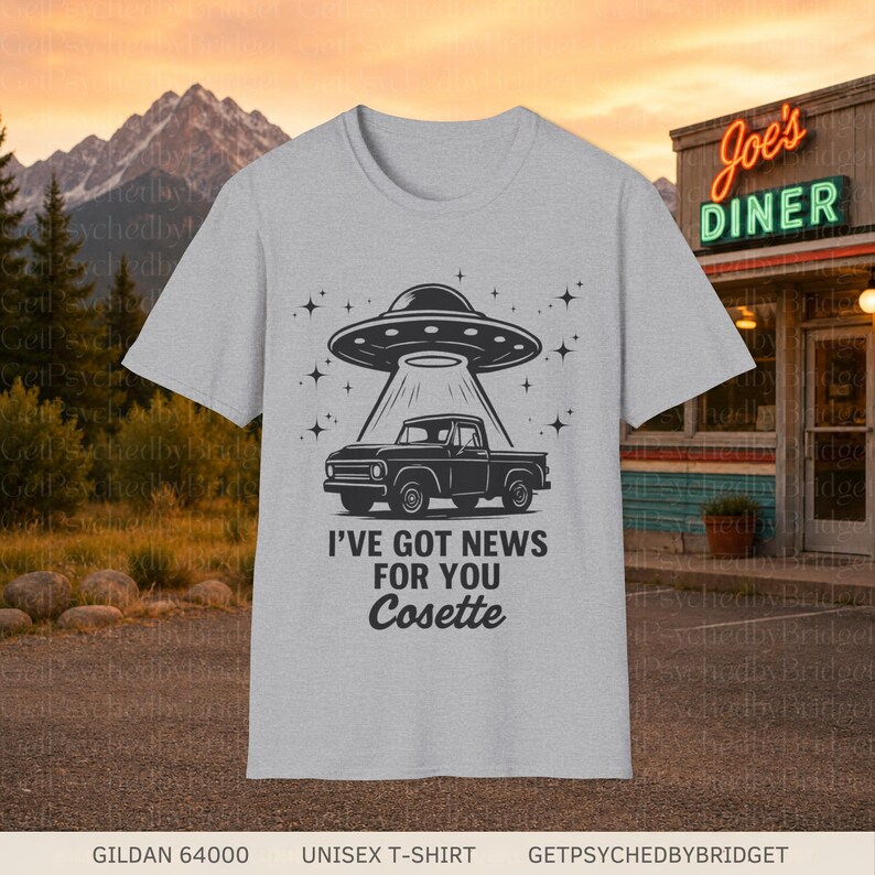 May include: A light gray t-shirt featuring a black graphic of a pickup truck being lifted by a UFO. The design includes stars and the text I'VE GOT NEWS FOR YOU Cosette printed in a bold, sans-serif font with the name in a script typeface.