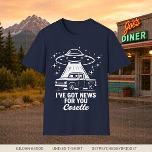 May include: A navy blue t-shirt featuring a white graphic of a pickup truck being abducted by a UFO. Below the truck, the text reads "I'VE GOT NEWS FOR YOU Cosette" in a bold, white, sans-serif font with the name in a script typeface.