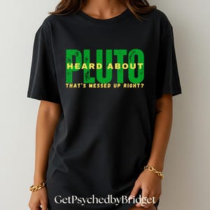 May include: Black t-shirt with green and yellow text that reads "Pluto Heard About That's Messed Up Right?"