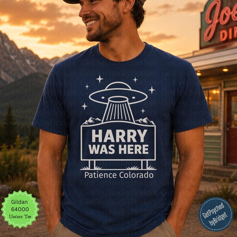 May include: A dark blue short-sleeve t-shirt featuring a white graphic of a UFO hovering over a rectangular sign that reads HARRY WAS HERE with the text Patience Colorado below it, surrounded by small star icons and mountain silhouettes.