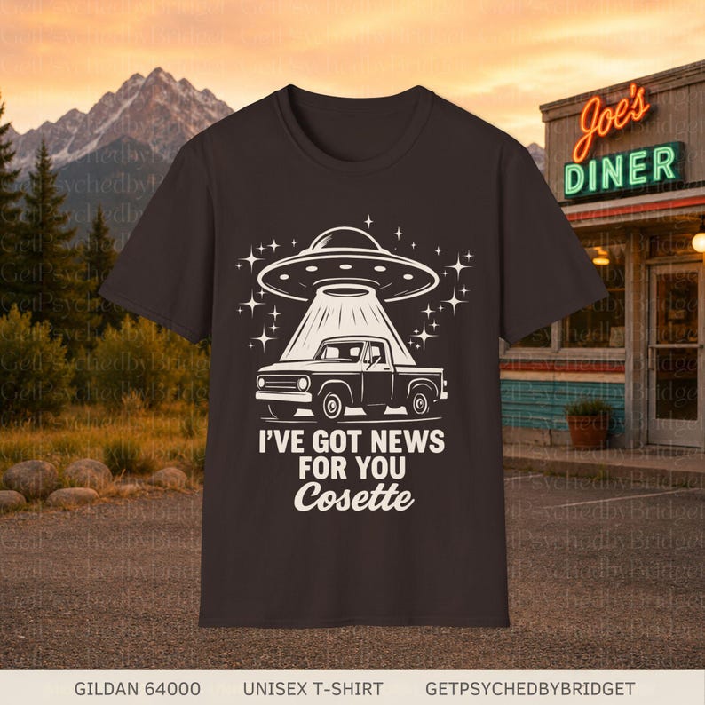 May include: A dark brown short-sleeve t-shirt featuring a white graphic of a pickup truck being beamed up by a UFO. The text reads I'VE GOT NEWS FOR YOU Cosette. The design includes star accents surrounding the flying saucer and the truck.