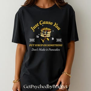 May include: Black t-shirt with a yellow graphic of a cartoon pancake with the text "Just Cause You Put Syrup On Something Don't Make It Pancakes".