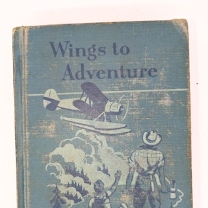 May include: Vintage book cover titled "Wings to Adventure" in blue. The cover features an illustration of a seaplane, a person waving, and another person holding an axe. The book has a worn appearance.