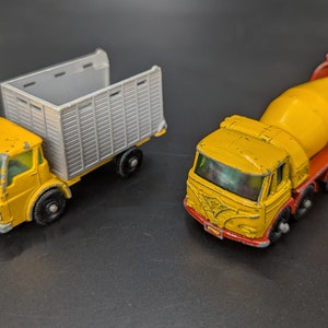 May include: Two vintage toy trucks. One is a yellow truck with a silver cargo bed. The other is a yellow cement mixer truck with a red chassis and a yellow drum. Both are on a dark surface.