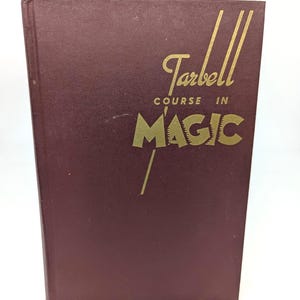 May include: A maroon hardcover book titled Tarbell Course in Magic with gold lettering on the front cover. The text is arranged with the word Tarbell in script above the words Course in and the large, bold, capitalized word MAGIC below.