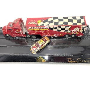 May include: A red McDonald's Racing Team semi-truck and race car set on a black display base. The truck features a checkerboard pattern and the Happy Meal logo. The race car is gold and red with the number 94.