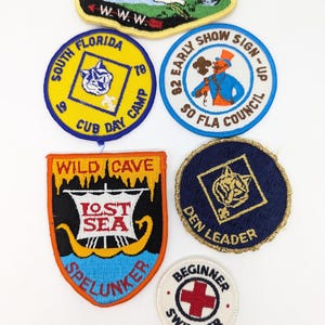 May include: A collection of vintage embroidered patches with various designs and text. Patches include "Shot Cain Lodge", "South Florida Cub Day Camp", "Early Show Sign-Up", "Lost Sea Spelunker", "Den Leader", and "Beginner Swimmer".