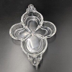 May include: A clear glass dish with a four-leaf clover design. The dish has a raised edge and a smooth, polished surface.