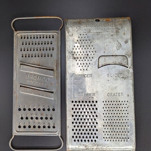 May include: Two vintage metal kitchen graters. One is rectangular with a handle and the word "BROMCO" printed on it. The other is a multi-purpose grater with "STREAMLINE UTILITY CUTTER" and the functions "MINCER", "SLICER", "SHREDDER", and "GRATER" printed on it.