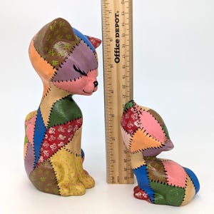 May include: Two colorful ceramic cat figurines. The larger cat is approximately 6 inches tall, and the smaller cat is about 3 inches tall. Each cat is made of patchwork-style pieces in various colors, including pink, blue, green, and yellow.