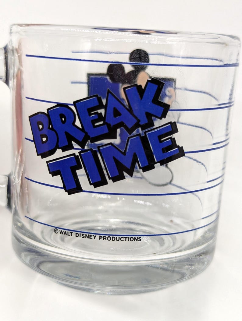 May include: Clear glass mug with the words "BREAK TIME" in blue block letters. The mug features a cartoon image of Mickey Mouse and blue horizontal lines. The text "WALT DISNEY PRODUCTIONS" is printed at the bottom.
