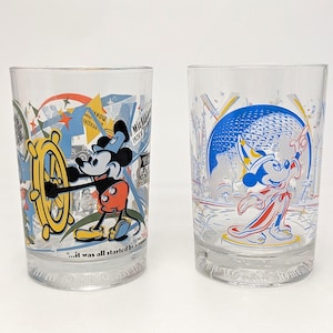 May include: Two clear drinking glasses with colorful Mickey Mouse designs. One glass features Mickey at the helm of a ship, the other shows Mickey in a sorcerer's outfit. Both glasses have a vintage aesthetic.