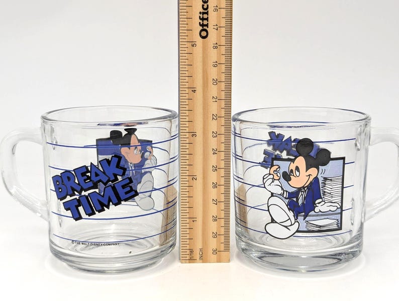 May include: Two clear glass mugs with handles, each featuring a cartoon image of Mickey Mouse in a blue suit. One mug has the words "BREAK TIME" in blue. The mugs have blue horizontal lines and are approximately 3 inches tall.