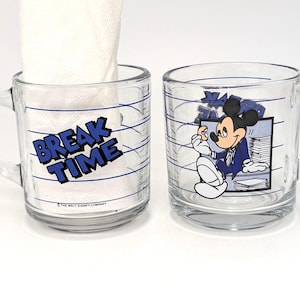 May include: Two clear glass mugs with handles. One mug has the words "BREAK TIME" in blue and white. The other mug features a cartoon image of Mickey Mouse in a blue suit. Both mugs have blue horizontal lines.