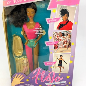 May include: A FloJo Florence Griffith Joyner fashion doll in a pink and teal leotard with one pink leg, packaged in a box with text including Let Your Dreams Run Free, Fashion, Fitness, Fantasy, and a set of nail stickers with a 11 1/2 inch size label.