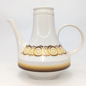 May include: A white ceramic coffee pot with a gold decorative band and a brown gradient at the base. The pot has a spout, a handle, and a lid. The design is vintage and elegant.