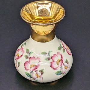 May include: A small white ceramic vase with a gold rim and a floral pattern of pink flowers and green leaves.