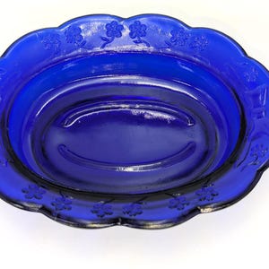 May include: A vibrant cobalt blue glass serving dish with a scalloped edge. The rim features embossed floral designs. The oval-shaped dish is ideal for serving food or as a decorative piece. The dish is made of glass.