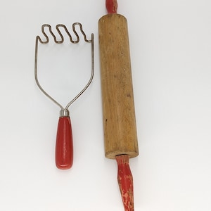 May include: A red handled potato masher and a wooden rolling pin with red handles.