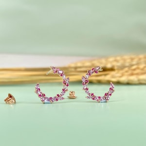 May include: A pair of gold hoop earrings with pink and white gemstones. The earrings are in the shape of a crescent moon.