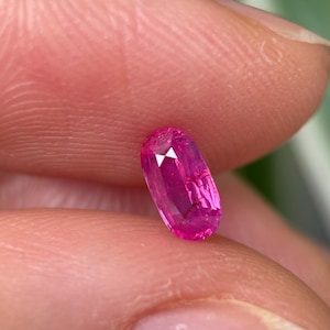 Könnte beinhalten: Ein leuchtend rosa ovaler Edelstein mit facettiertem Schliff. Der Edelstein wird in einer Hand gehalten.
