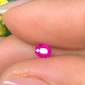 Può includere: Una gemma rosa acceso, taglio ovale, vibrante. La gemma è tenuta tra due dita, mostrando le sue sfaccettature lucide e la sua brillantezza interna. Il colore della pietra è un rosa intenso e saturo, che riflette la luce. Questa gemma è probabilmente per la creazione di gioielli.