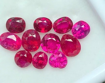 May include: A collection of faceted, oval and pear-shaped rubies in varying shades of red and pink. The gemstones are displayed on a white surface, showcasing their brilliance and clarity. Ideal for jewelry making or gemstone collectors.