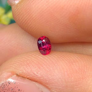 Peut inclure: Une petite pierre précieuse de taille ovale avec une couleur rouge profonde et vibrante et une surface à facettes qui reflète la lumière. La pierre est translucide, affichant une clarté interne et une teinte saturée et brillante.