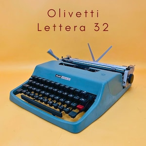 Może przedstawiać: Niebieska przenośna maszyna do pisania Olivetti Lettera 32 z czarnymi klawiszami, jednym czerwonym klawiszem i metalowym wózkiem. Tekst Olivetti Lettera 32 znajduje się nad maszyną. Posiada dźwignię powrotu wózka oraz wspornik papieru.