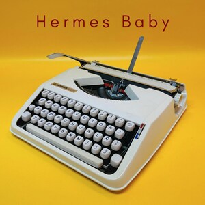 Puede incluir: Una máquina de escribir Hermes Baby blanca con un teclado completo y un soporte de papel plateado. La máquina de escribir está sobre un fondo amarillo brillante, con las palabras "Hermes Baby" en rojo en la parte superior.