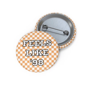 May include: Orange and white checkered button with the text "Feels Like '98" in black and white.