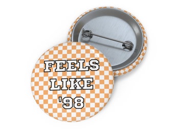 May include: Orange and white checkered button with the text "Feels Like '98" in black and white.