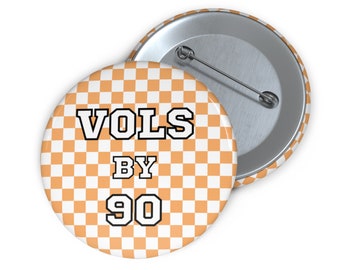 Könnte beinhalten: Orange-weißer Schachbrett-Knopf mit dem Text "VOLS BY 90" in Schwarz und Weiß.