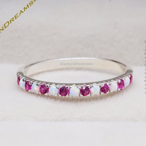 May include: A silver band ring featuring a row of white opal and pink ruby gemstones. The ring is displayed in a white box with the text "DiamondDreams4u" on the side.