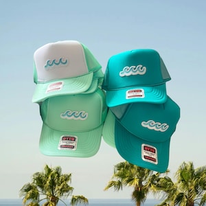 May include: Four trucker hats stacked together, featuring a white and mint green cap, a solid mint green cap, and two solid teal caps. Each hat displays an embroidered light blue wave graphic on the front and an Otto brand sticker on the brim.
