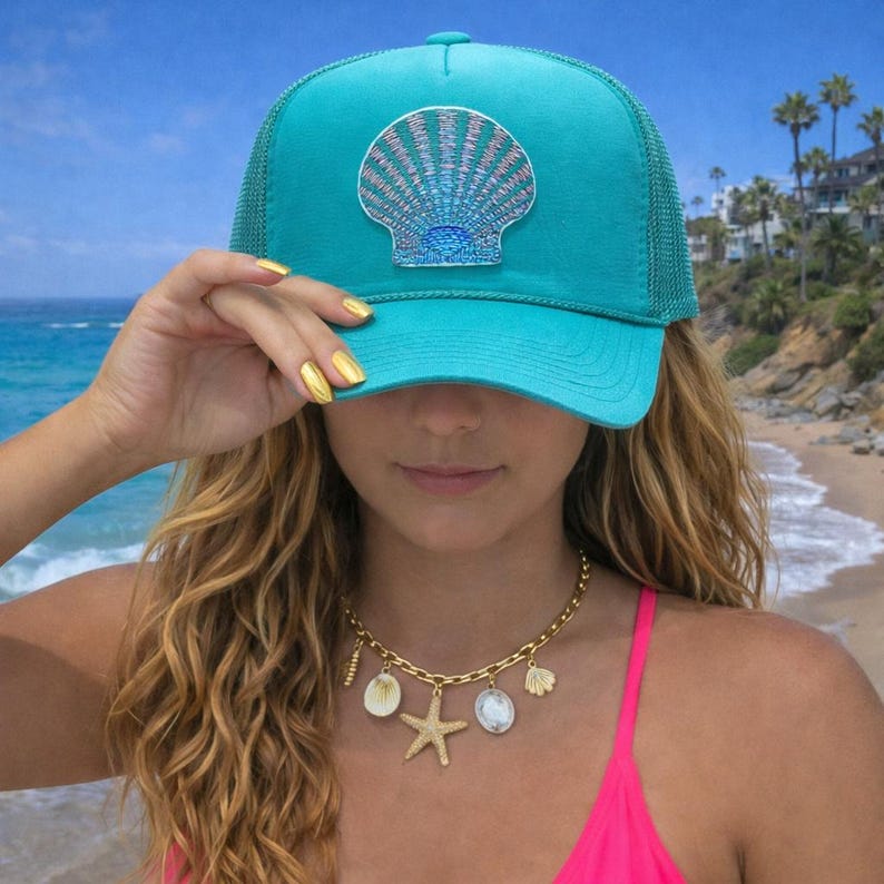 May include: A turquoise trucker hat with a seashell patch. The hat has a mesh back and a curved brim. A gold necklace with seashell charms and a starfish pendant is also visible.