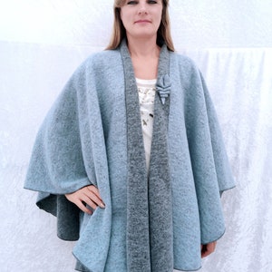 May include: A light blue and grey wool cape with a decorative flower brooch. The cape has a shawl collar and a flowing design.