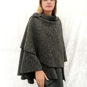 May include: A grey wool poncho with a ruffled hem and a decorative button on the shoulder.