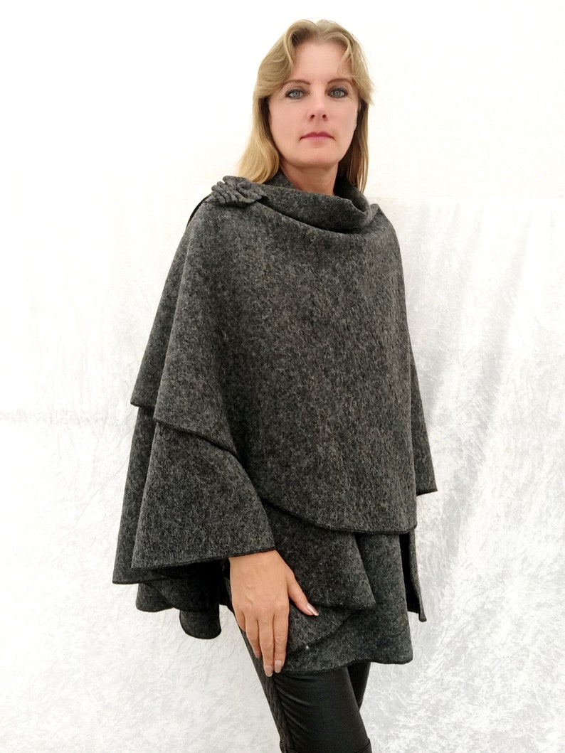 May include: A grey wool poncho with a ruffled hem and a decorative button on the shoulder.