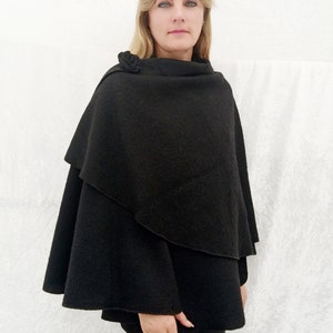 May include: A black wool cape with a cowl neck and a decorative button detail. The cape is draped over the shoulders and falls to mid-thigh.