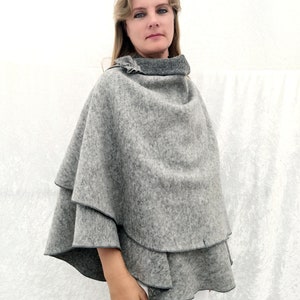 May include: A grey wool poncho with a ruffled neckline. The poncho is layered and has a slightly flared shape.