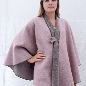 May include: A mauve-coloured cape with a grey trim and a grey tie closure. The cape is made of a soft, fuzzy material.