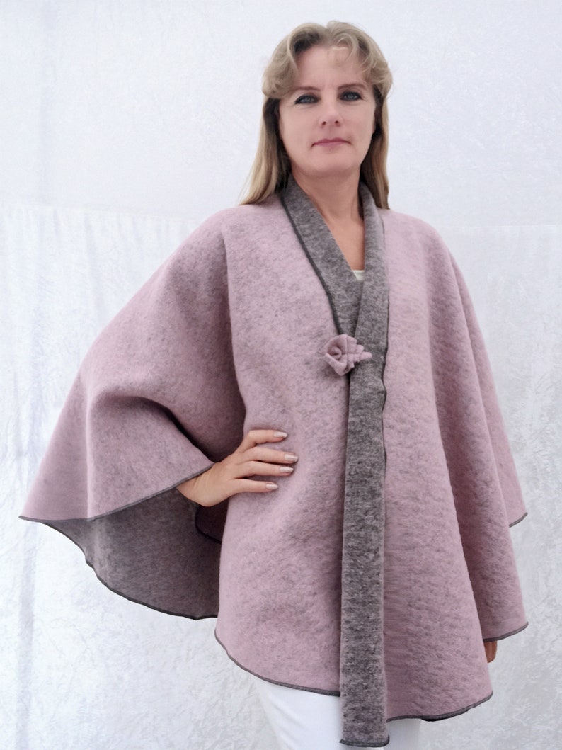 May include: A mauve-coloured cape with a grey trim and a grey tie closure. The cape is made of a soft, fuzzy material.